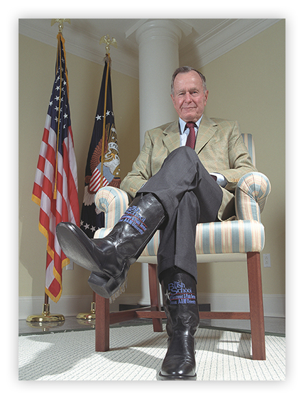 President Bush sitting in a chair wearing his Bush School engraved cowboy boots