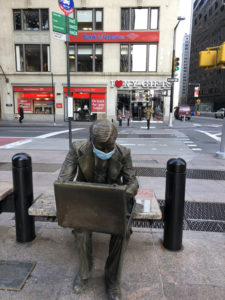 Statue of a man sitting on a bench with a mask over his nose and mouth in New York City