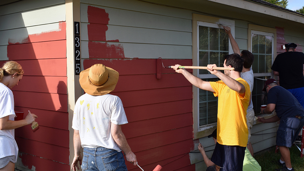 Students working high and low to paint the side of a Habitat for Humanity House