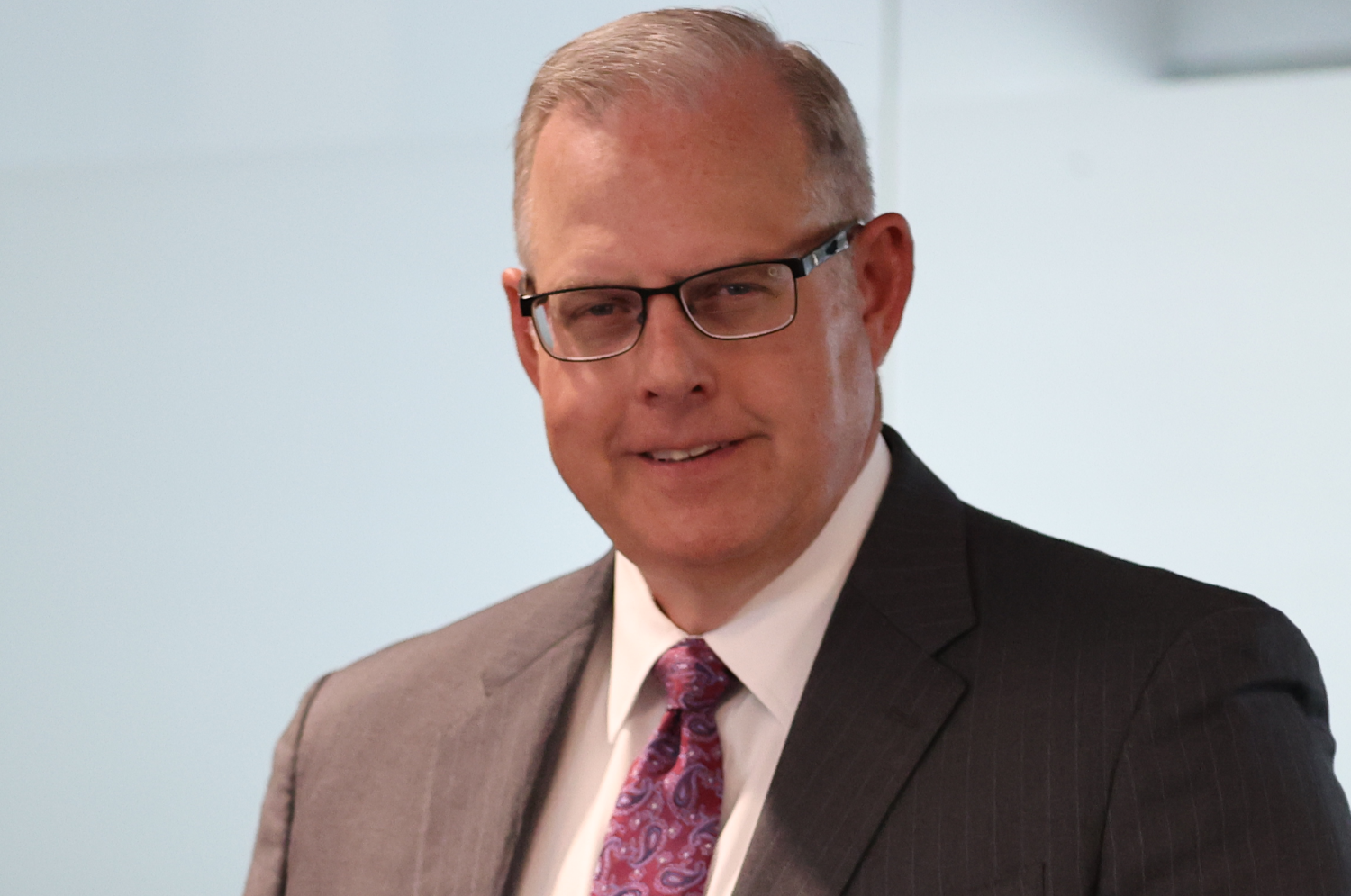 A head-and-shoulders photo of John Sherman, dean of The Bush School of Government and Public Service. Sherman is smiling, wearing a suit with an Aggie-red tie.
