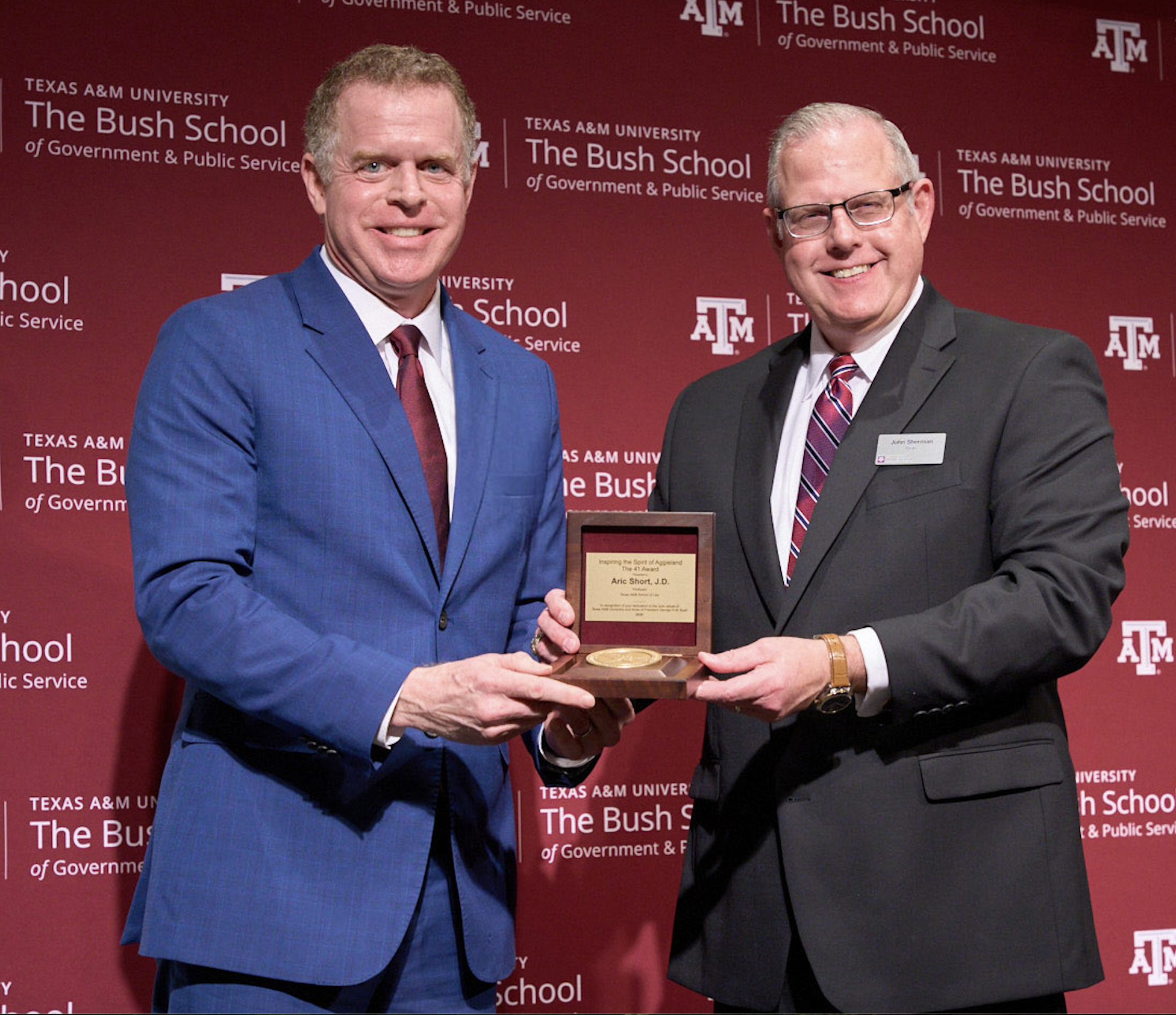 Aric Short and Bush School Dean John Sherman jointly hold up the 41 Award. Both are wearing suits, smiling and looking toward the camera.