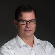 A photo of Clifford Young, Ph.D., from the waist up. He is wearing a white dress shirt, his arms are crossed and he has serious, professional expression.